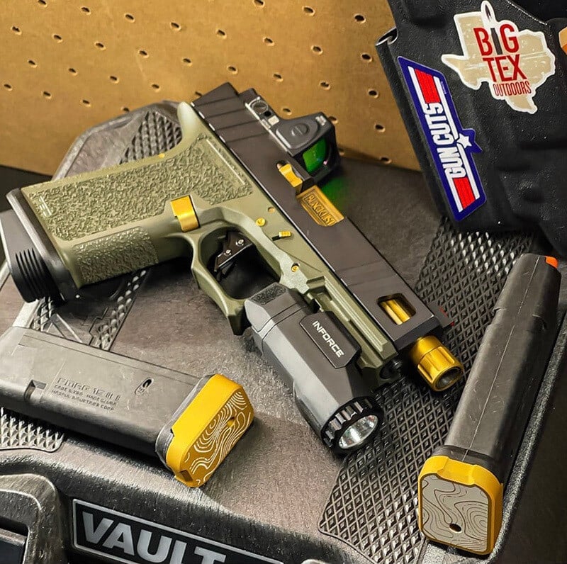 Apprentice slide in OD green with a gold barrel, set in a pistol vault with a light and spare magazines