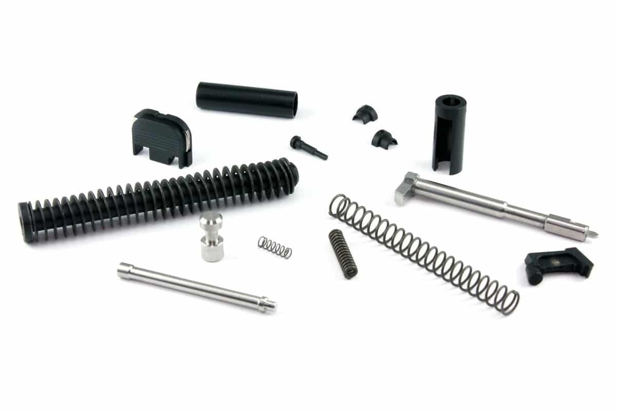Glock 19 upper parts kit laid out on white: recoil spring assembly, striker, channel liner, extractor and pins