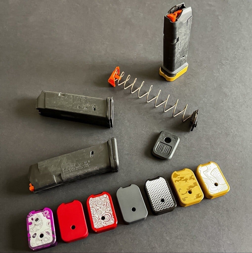 Row of aluminum magazine base plates in pink, red, grey, gold and black, with magazines and springs