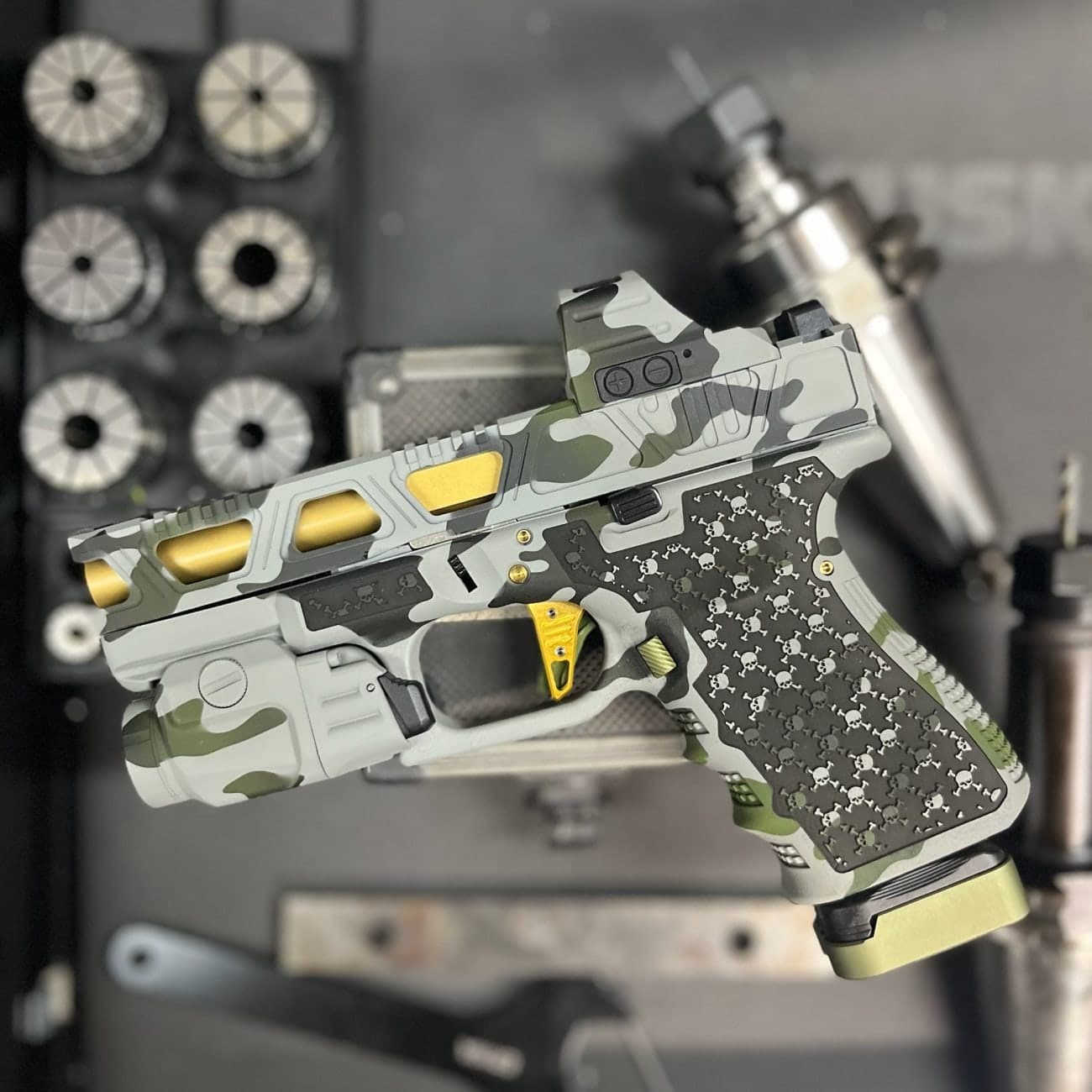 Camo Cerakoted pistol resting on the bench in front of a rack of CNC tool holders